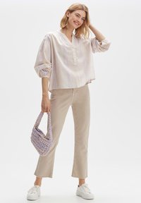 Blusa chiara, a righe, morbida con scollatura a V e tre bottoni, abbinata a pantaloni beige a campana e una borsa intrecciata lavanda.