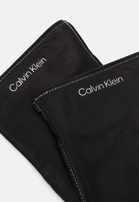 Guanti in pelle nera con cuciture bianche e marchio "Calvin Klein" su ciascuno. Texture liscia, design elegante e forma attillata.