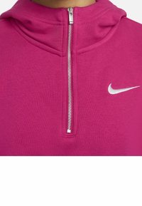 Fuchsias zip-up hoodie med hög krage, med en silverdragkedja och en vit Nike-logotyp på vänster sida. Slät tygtextur.