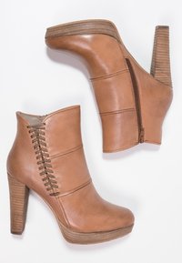 Bottes en cuir marron à cheville avec un talon haut texturé et une plateforme. Présente des coutures décoratives et une fermeture éclair sur le côté.