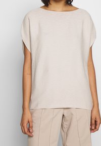 Beige kortärmad topp med en vid halsringning och textilerad tyg, i kombination med ljusa, skräddarsydda byxor. Enkelt design, inga synliga mönster.