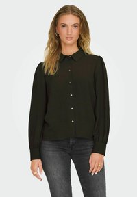 Zwarte blouse met lange mouwen, voorzien van een kraag, knoopsluiting, zachte textuur en puffed schouders, gecombineerd met donkere jeans.