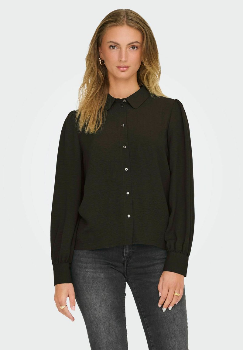 Zwarte blouse met lange mouwen, voorzien van een kraag, knoopsluiting, zachte textuur en puffed schouders, gecombineerd met donkere jeans.