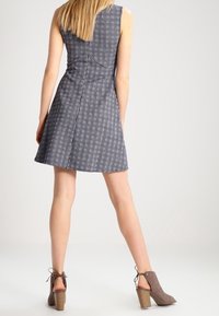 Robe sans manches à carreaux bleu marine et blanc, corsage ajusté avec jupe évasée. Associée à des bottines grises à talon empilé.