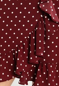 Tissu bordeaux avec des pois blancs, texturé avec des volants superposés le long du bord d'un vêtement.