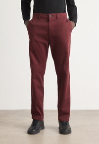 Pantalon en coton bordeaux avec une coupe droite, poches avant et fermeture à bouton, associé à des baskets noires.