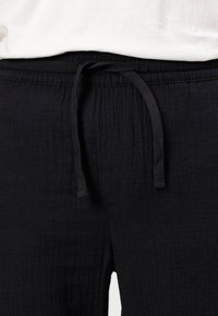 Czarne lekkie spodnie dresowe z elastycznym pasem i sznurkiem do regulacji. Tkanina ma fakturowane wykończenie, a krój jest luźny, z kieszeniami po bokach.