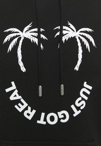 Black hoodie featuring two white palm tree graphics; "JUST GOT REAL" text in white beneath, with silver aglets on drawstrings.