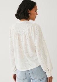Blusa bianca a maniche lunghe con motivo a occhio di diamante, tessuto testurizzato, dettagli arricciati sul retro e polsini elasticizzati.