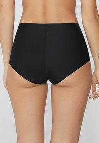Schwarze, hoch geschnittene Badehosen aus glattem, dehnbarem Material. Nahtdetails verlaufen vertikal in der Mitte des Rückens. Vollständige Bedeckung.