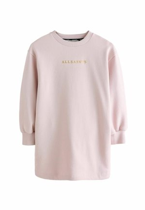 Person iført en lyserød oversized sweatshirt-kjole med gyldent "AllSaints"-tekst, hvide sokker med sort tekst og hvide sneakers.