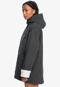 Čierna kapucňová bunda s voľným strihom, ktorá má biely šerpa podšitý manžetou a prednú kapsu. Textúrovaná tkanina s hladkým povrchom.