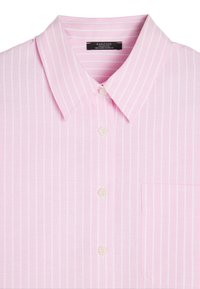 Jasnoróżowa koszula z krótkim rękawem, w białe pionowe paski, z kołnierzykiem, czterema guzikami i kieszonką na piersi. Wykonana z bawełnianej tkaniny o gładkiej teksturze.