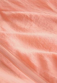 Tissu doux de couleur corail avec une couture visible et des plis subtils, mettant en valeur la texture et les détails de la couture.