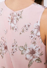 Roze mouwloos topje met bloemenpatronen in het wit en bruin. Heeft een ronde halslijn en een kleine sleutelgatsluiting op de rug.