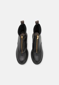 Zwarte leren enkellaarzen met een ronde neus, gouden ritsdetails en bruine textuuraccenten aan de bovenkant. Dikke zool met stiksels.