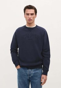 Marineblauwe katoen sweatshirt met een ronde hals en raglanmouwen. Voorzien van het verhoogde logo "SCALPERS THEATRE" op de voorkant. Gecombineerd met blauwe jeans.