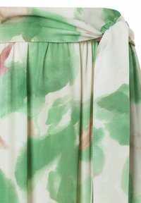 Tissu fleuri vert et blanc avec une texture douce et fluide. Présente un détail de taille nouée et des plis froncés en haut.