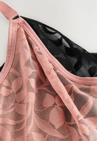 Lingerie-top met een zwart doorschijnend kantontwerp met een bloemenpatroon, aangevuld met een effen roze stoffen bies langs de halslijn en schouderband.