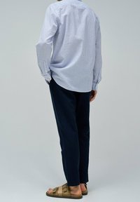 Camicia a righe blu e bianca con bottoni, pantaloni blu scuro e sandali marroni con cinturini; vestibilità casual, tessuto leggero, silhouette rilassata.
