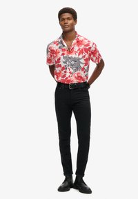 Korte mouw bloemige shirt in rode, roze en zwarte patronen; gecombineerd met zwarte aansluitende jeans en zwarte veterschoenen.