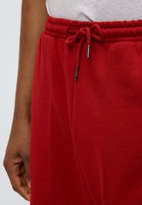 Κόκκινο φούτερ παντελόνι από παχύ ύφασμα, με ελαστική μέση και κορδόνι, πλαϊνές τσέπες και λείο υφή.