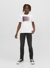 Camiseta blanca con un diseño gráfico que presenta "JACK & JONES" en rojo, combinada con jeans negros y zapatillas negras con toques blancos.