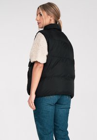 Czarna pikowana kamizelka z wysokim kołnierzem i kremowymi, teksturowanymi rękawami, stylizowana z jasnoniebieskimi, wysokim stanem dżinsami, przedstawiająca widoki z tyłu i z boku.