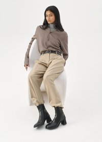 Cămașă maro cu nasturi, pulover gri cu guler, pantaloni bej, cizme negre până la gleznă. Material neted, croială lejeră, talie înaltă și tocuri pătrate.