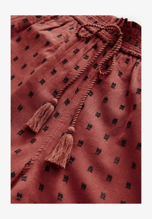 Lyhythihaiset ruskoraidalliset shortsit, joissa on kiristettävä vyötärö ja mustia brodeerattuja kuvioita sekä tupsuaiheita naruissa. Pehmeä, teksturoitu kangas.