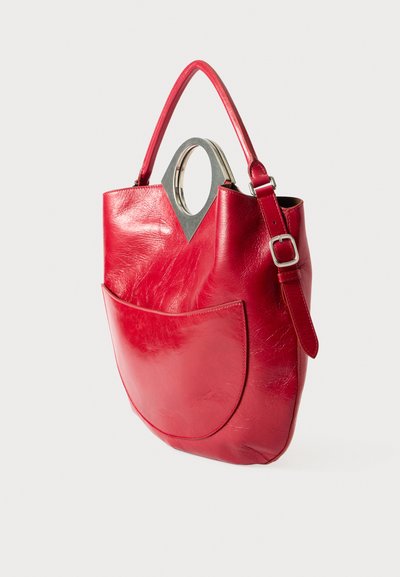Sac à main en cuir rouge avec une poignée arrondie distinctive, une poche plate à l'avant et une texture lisse, légèrement brillante. Bandoulière ajustable incluse.