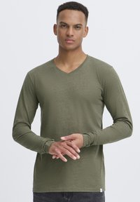 Langärmliges, olivgrünes V-Ausschnitt-T-Shirt aus weichem, strukturiertem Stoff, mit enganliegenden Ärmeln und einem kleinen Etikett am unteren Rand.
