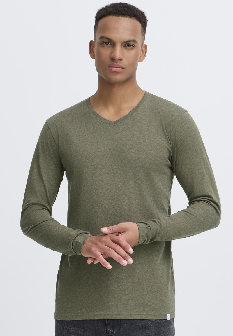 Langärmliges, olivgrünes V-Ausschnitt-T-Shirt aus weichem, strukturiertem Stoff, mit enganliegenden Ärmeln und einem kleinen Etikett am unteren Rand.