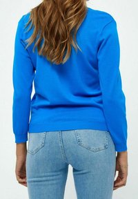 Pull tricot bleu à manches longues avec poignets côtelés, associé à un jean bleu clair présentant un design classique de poche.