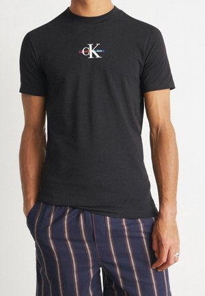 Schwarzes Baumwoll-T-Shirt mit einem weißen "CK"-Logo und buntem "Calvin Klein Jeans"-Schriftzug darunter. Kurzarm und Rundhalsausschnitt.