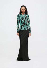 A camisa de botão de manga longa apresenta um padrão floral em turquesa e preto. O modelo usa uma saia justa preta que se estende até o chão.