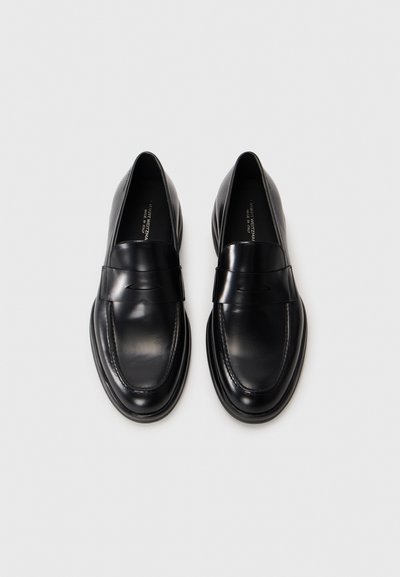 Svarta läderloafers med en slät matt finish, bred rem över fotryggen och stickad detalj runt tån och häl. Platt sula.