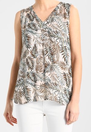 Blouse sans manches à col en V avec un motif de feuilles marron et gris, portée avec un pantalon blanc, vue des épaules jusqu'aux hanches.