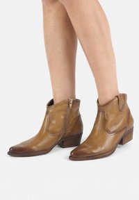 Botas de cuero marrón hasta el tobillo con puntera puntiaguda, cremallera lateral y costuras decorativas; tacón bajo y apilado. Textura suave con un acabado pulido.