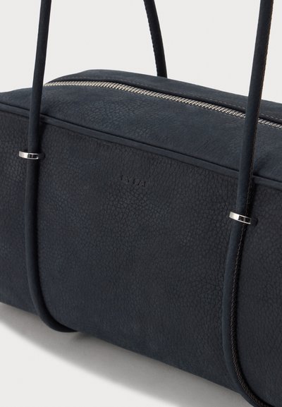 Sac à main noir texturé avec deux fines poignées ornées d'anneaux argentés et une fermeture éclair sur le dessus sur fond clair.
