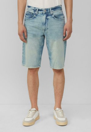 Shorts en denim bleu clair avec une coupe régulière, cinq poches, fermeture éclair et léger délavage. Associés à des baskets blanches et beiges.