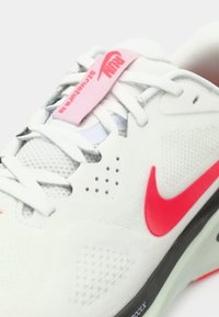 Λευκό αθλητικό παπούτσι με επάνω μέρος από διχτυωτό και ύφασμα, ροζ λογότυπο Nike, ροζ ετικέτα στη γλώσσα και ορατή cushioned σόλα με μαύρες λεπτομέρειες.