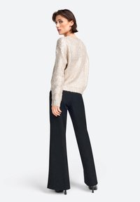 Hellbeige strukturierte Sweatjacke mit lockerer Passform, kombiniert mit hoch-taillierten schwarzen weit geschnittenen Hosen, von hinten gezeigt.