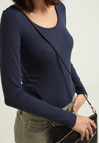 Marinblå långärmad topp med rundad halsringning, tillverkad av mjukt material, kombinerad med olivgröna byxor och en svart axelremsväska.