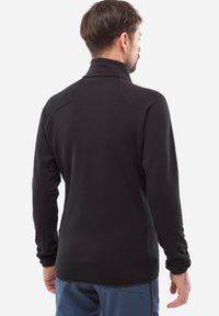 Pull noir à manches longues avec col haut, coupe slim et coutures plates, fabriqué à partir d'un matériau doux et extensible. Vue de dos présentée.