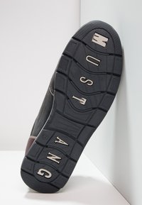 Semelle de chaussure en caoutchouc noir avec des rainures profondes. Présente des lettres métalliques "MUSTANG" et des rainures courbes pour l'adhérence. Fini robuste et texturé.