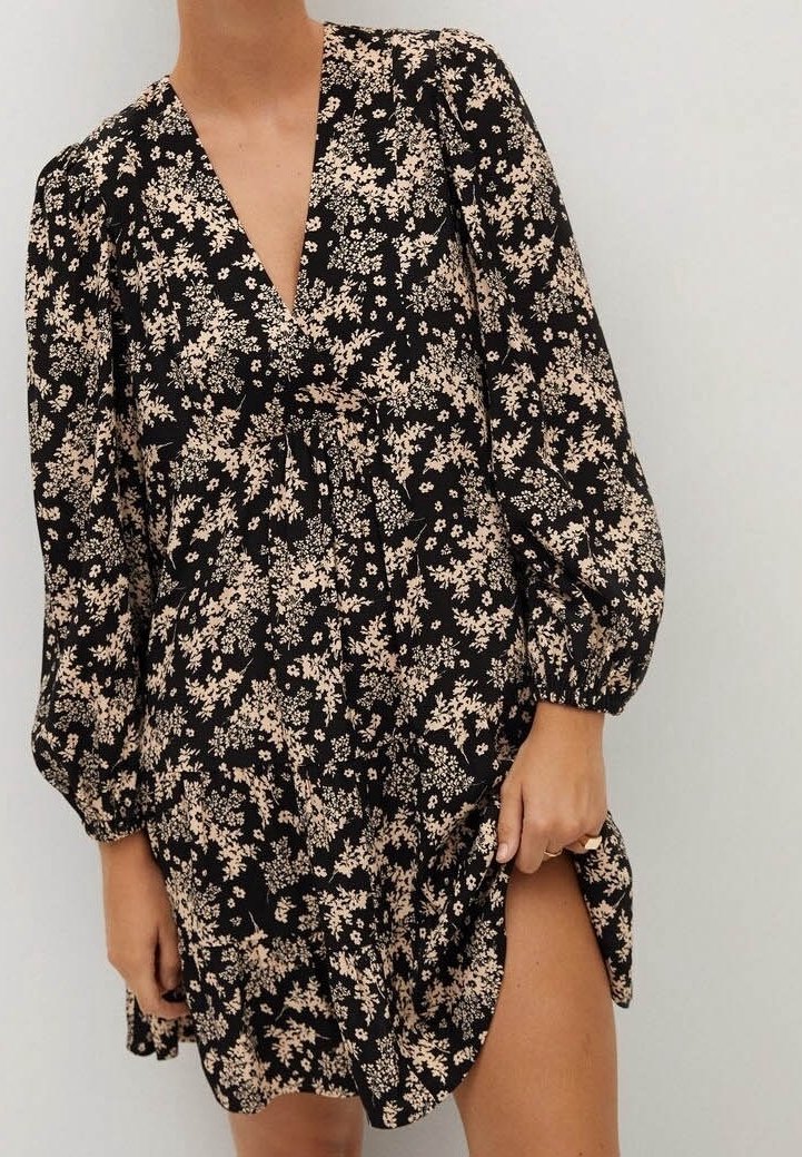 Schwarzes Blumenkleid mit langen Puffärmeln, tiefem V-Ausschnitt und hohem Schlitz, das mit kleinen beigen Blumen und einem weichen, fließenden Stoff ausgestattet ist.