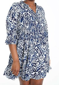 Marinblå och vit mönstrad skjortklänning med långa ärmar, knäppt halsringning och volangärmar. Tillverkad av lätt material med en lös passform.