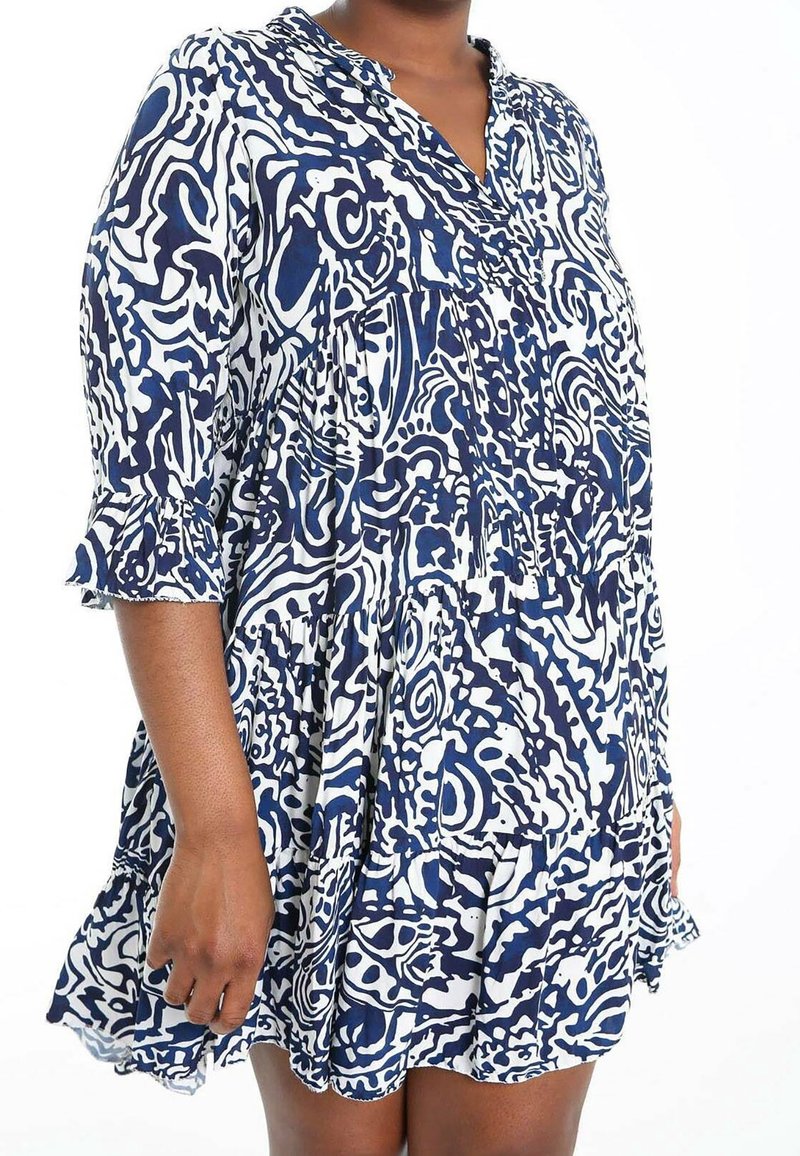 Marinblå och vit mönstrad skjortklänning med långa ärmar, knäppt halsringning och volangärmar. Tillverkad av lätt material med en lös passform.