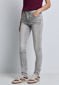 Jeans ajustados de color gris claro con una textura suave, diseño de cinco bolsillos y un ligero desgastado. Combinados con zapatillas casuales de rayas multicolores.